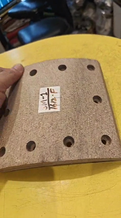 Rectangular sanding block with holes on a yellow surface, held by a hand.