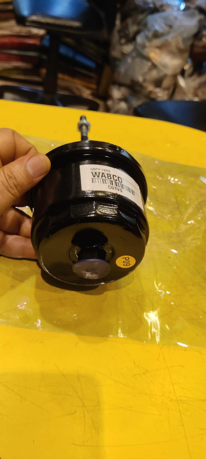 Hand holding a black cylindrical filter with a label on a yellow surface