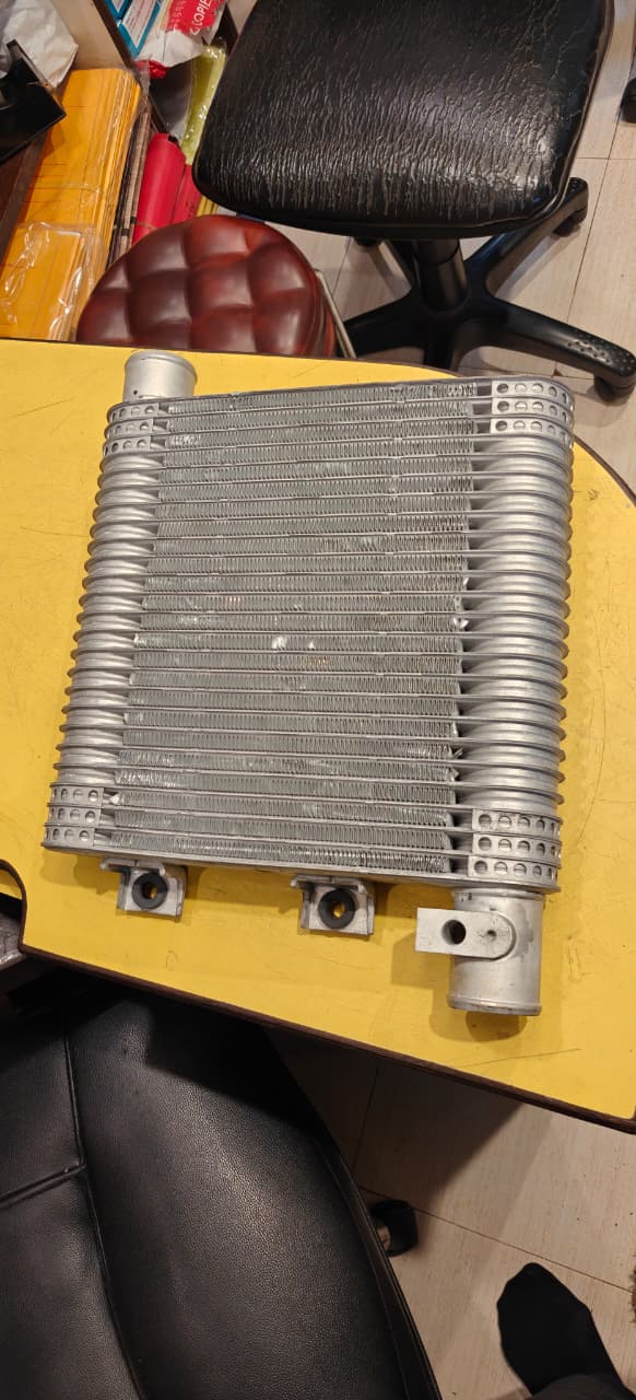 Metallic heat exchanger on a yellow surface with a chair and box in the background intercooler