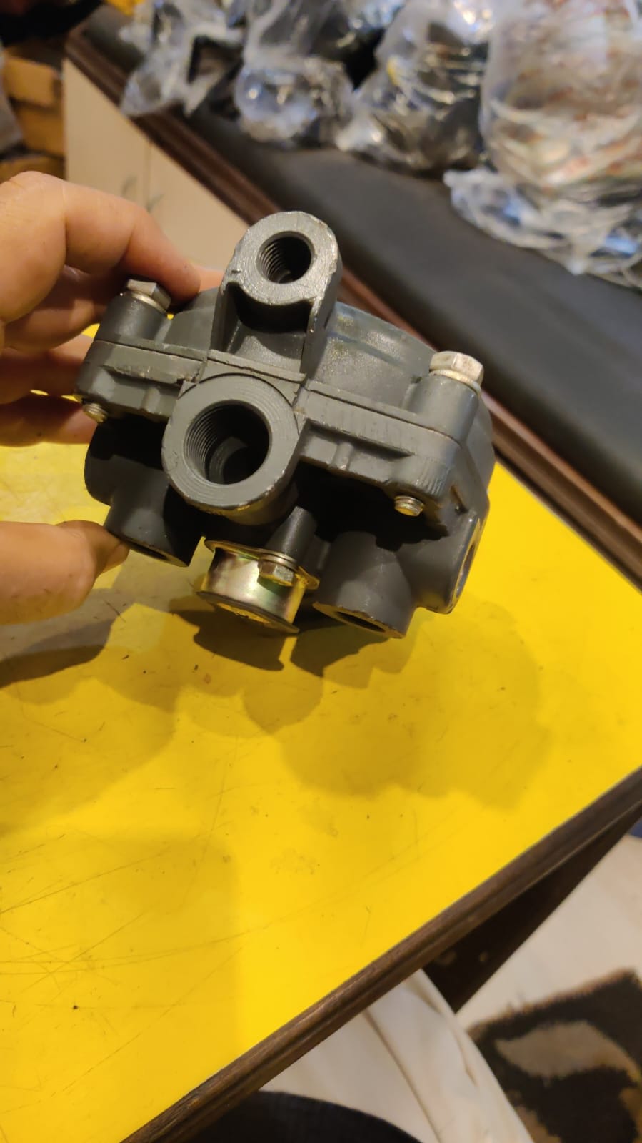 Mechanical part held by a hand on a yellow surface with blurred background