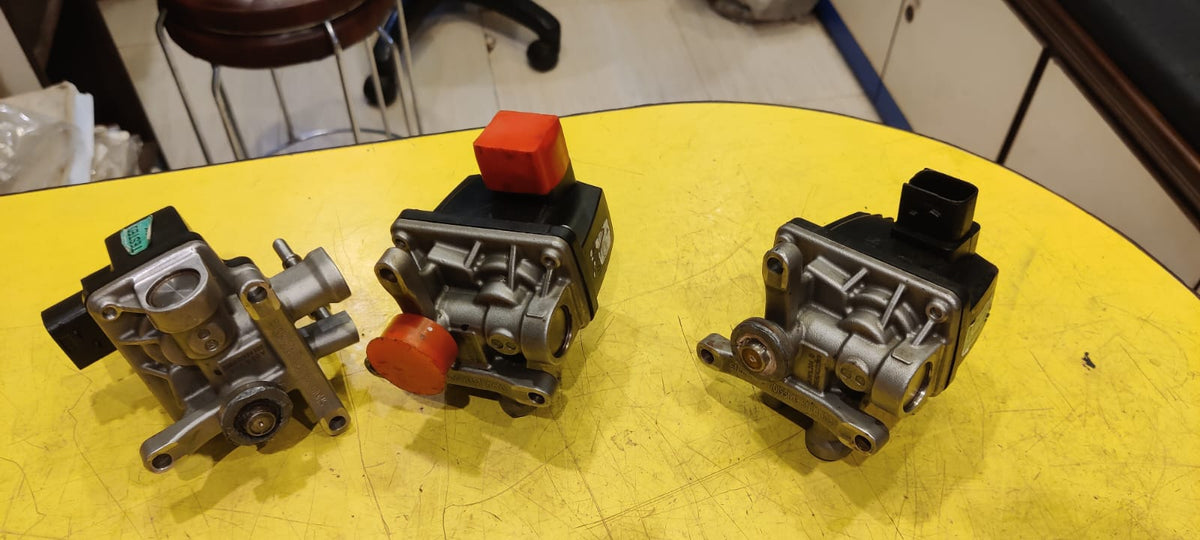 Three mechanical components on a yellow surface with a blurred background