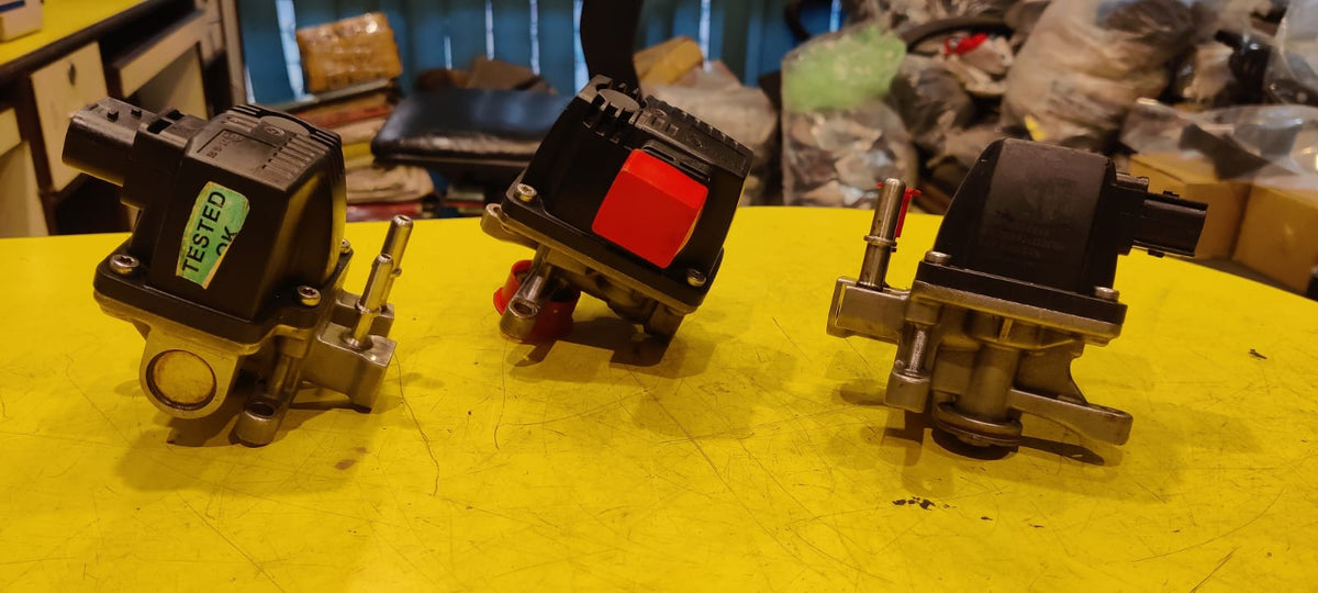 Three mechanical components on a yellow surface with a blurred background