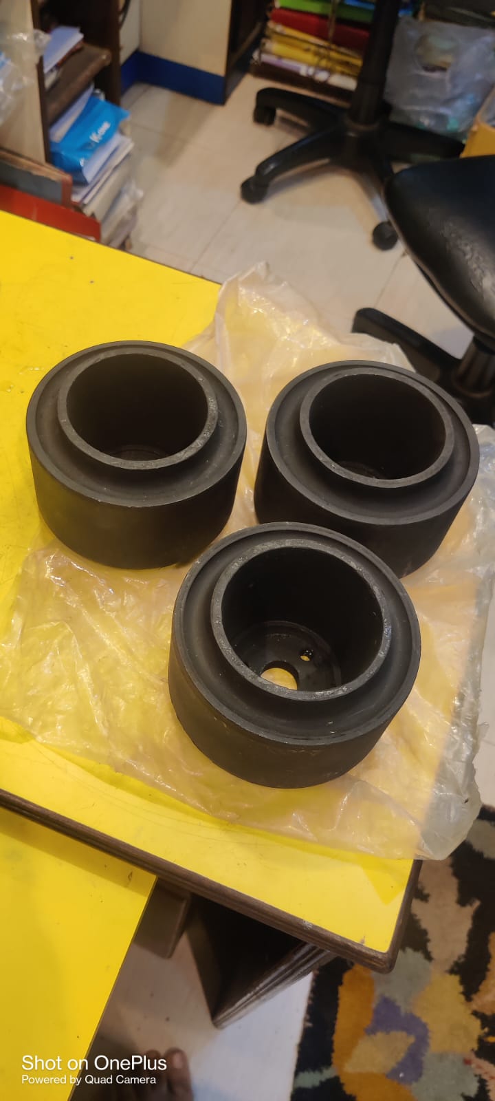 Three black rubber bushings on a yellow surface with office furniture in the background.