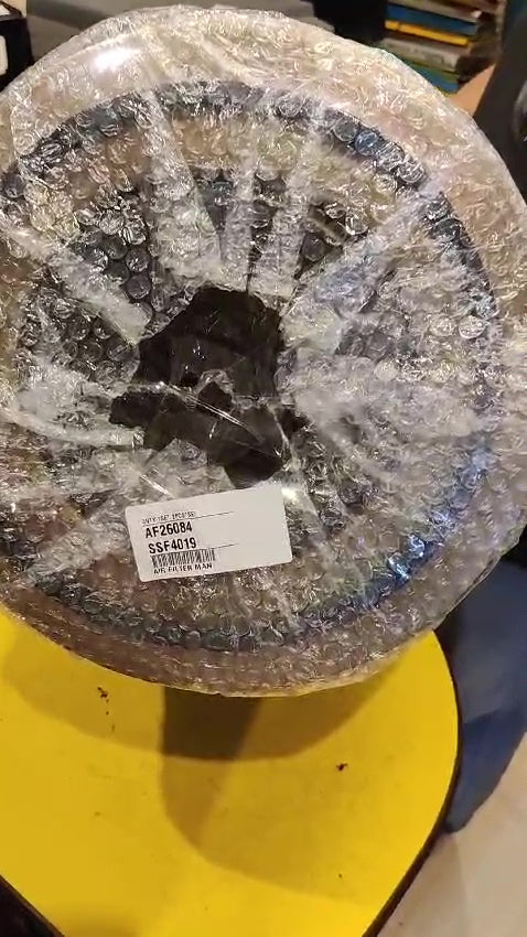 Round metallic object wrapped in plastic on a yellow surface
