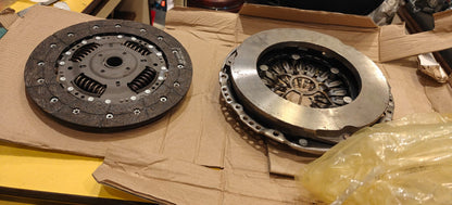 Two clutch plates on a cardboard surface with tools in the background
