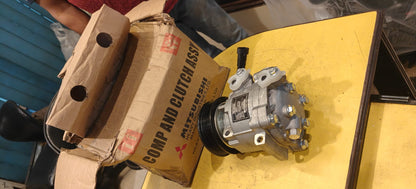 A mechanical component on a yellow surface next to a cardboard box with Mitsubishi branding.