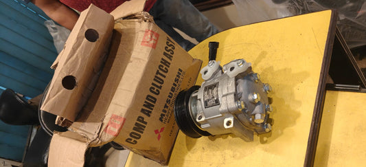 A mechanical component on a yellow surface next to a cardboard box with Mitsubishi branding.