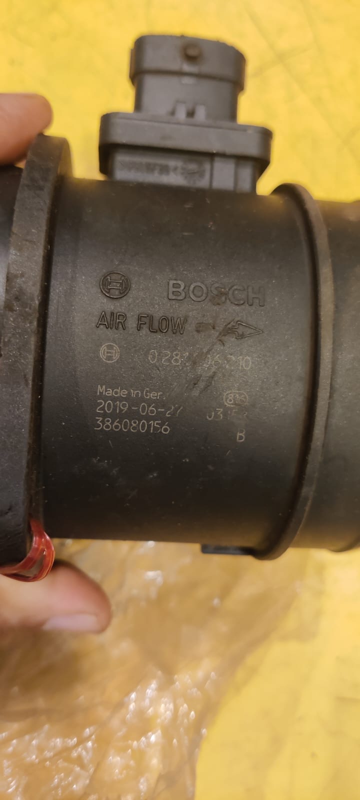 Bosch air flow sensor held by a hand on a yellow background