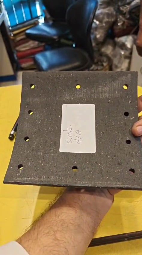 Square metal block with holes and a label held by a person on a yellow surface.