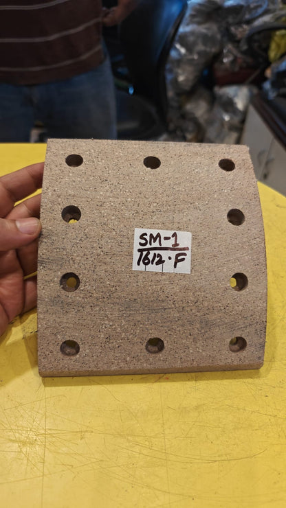 Square sandpaper sheet with holes held by a hand on a yellow surface