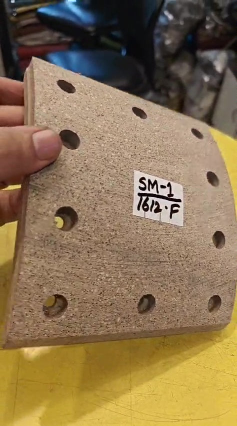Textured sanding block with holes, held by a hand, on a yellow surface.