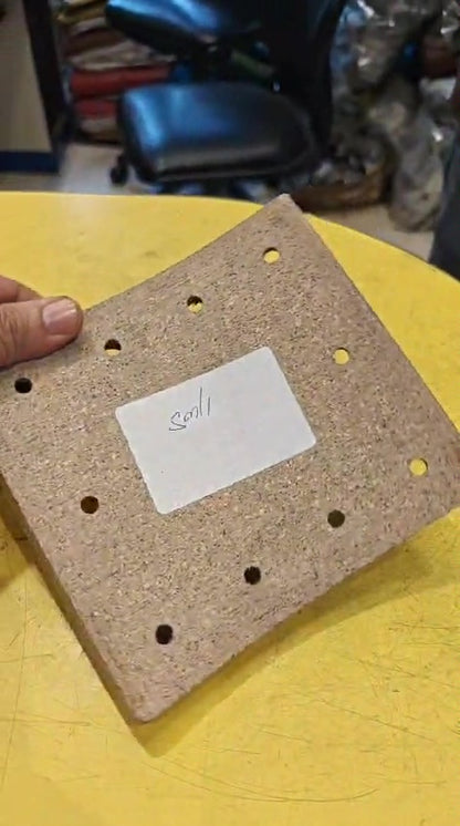 Cork board with holes on a yellow surface, held by a hand.