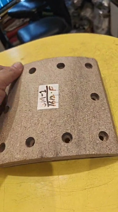 Rectangular sanding block with holes on a yellow surface, held by a hand.