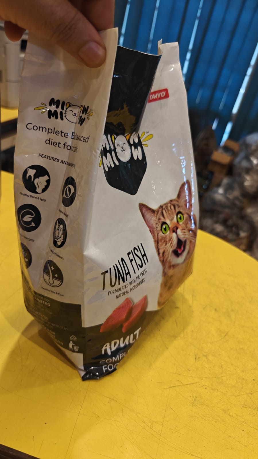 Two packages of Miao Miao cat food on a yellow surface with a blue background.