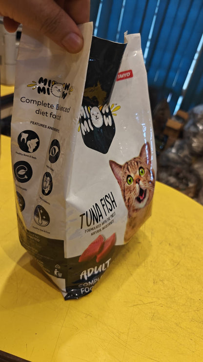 Two packages of Miao Miao cat food on a yellow surface with a blue background.