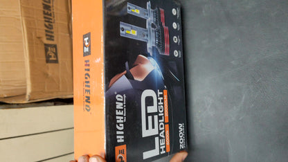 Highend LED Headlight packaging held by a hand on a concrete floor with cardboard boxes in the background.