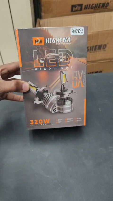 HighEnd LED headlight packaging held by a hand on a dark surface with cardboard boxes in the background.