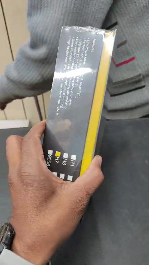 Person holding a rectangular product packaging with text and a yellow strip.