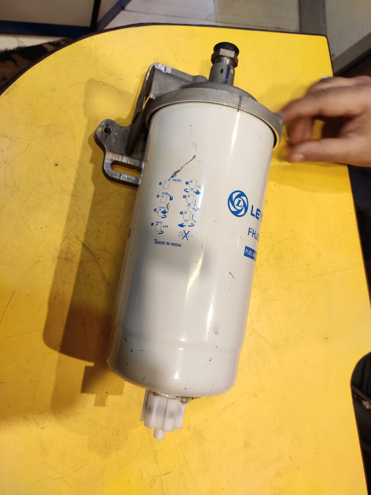 Fuel filter on a yellow surface with a hand reaching towards it