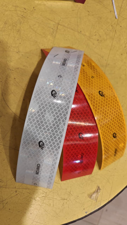 Three reflective safety stickers in red, yellow, and silver on a wooden surface.
