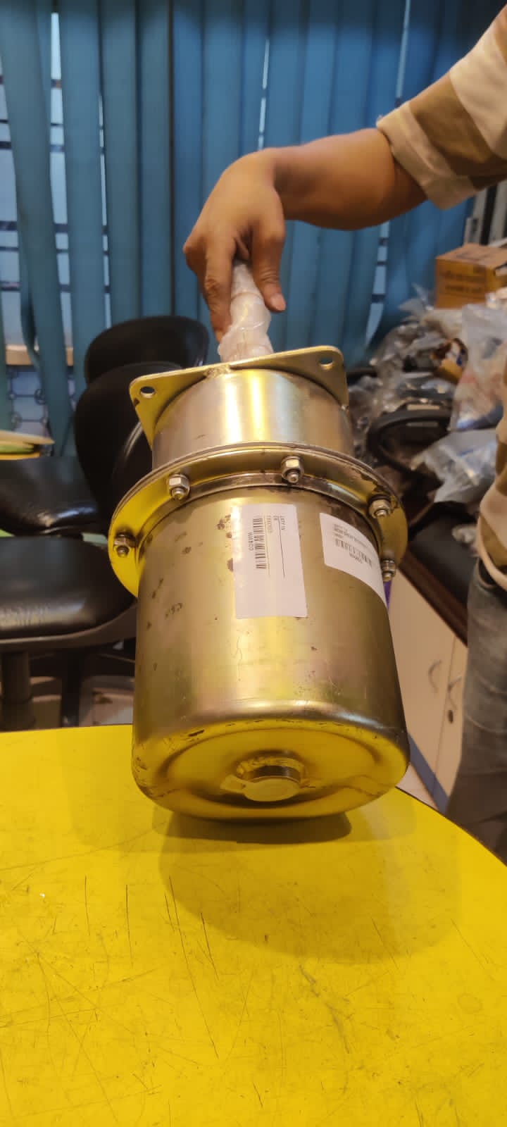 Gold-colored mechanical component on a yellow surface with a blurred background