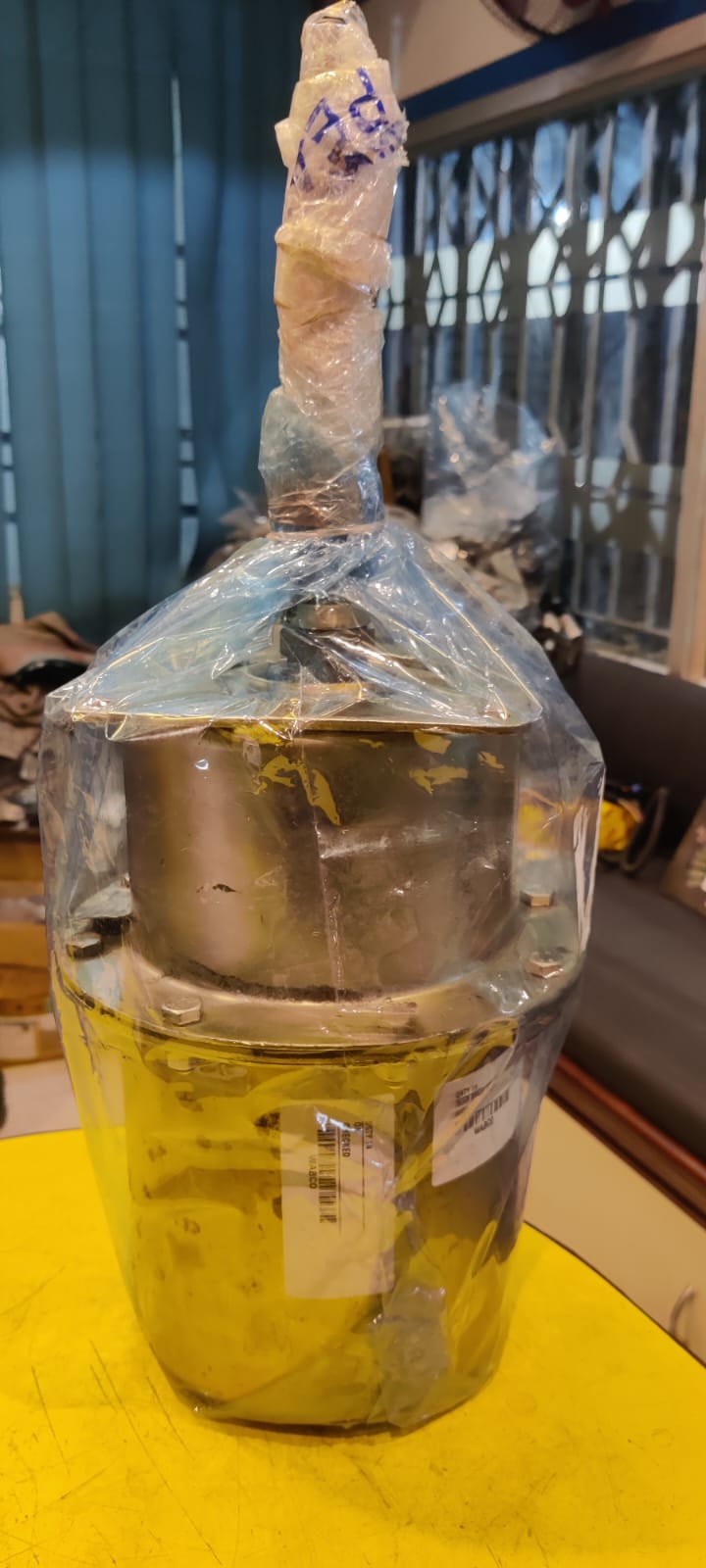 Metal container with a label inside a clear plastic bag on a yellow surface.