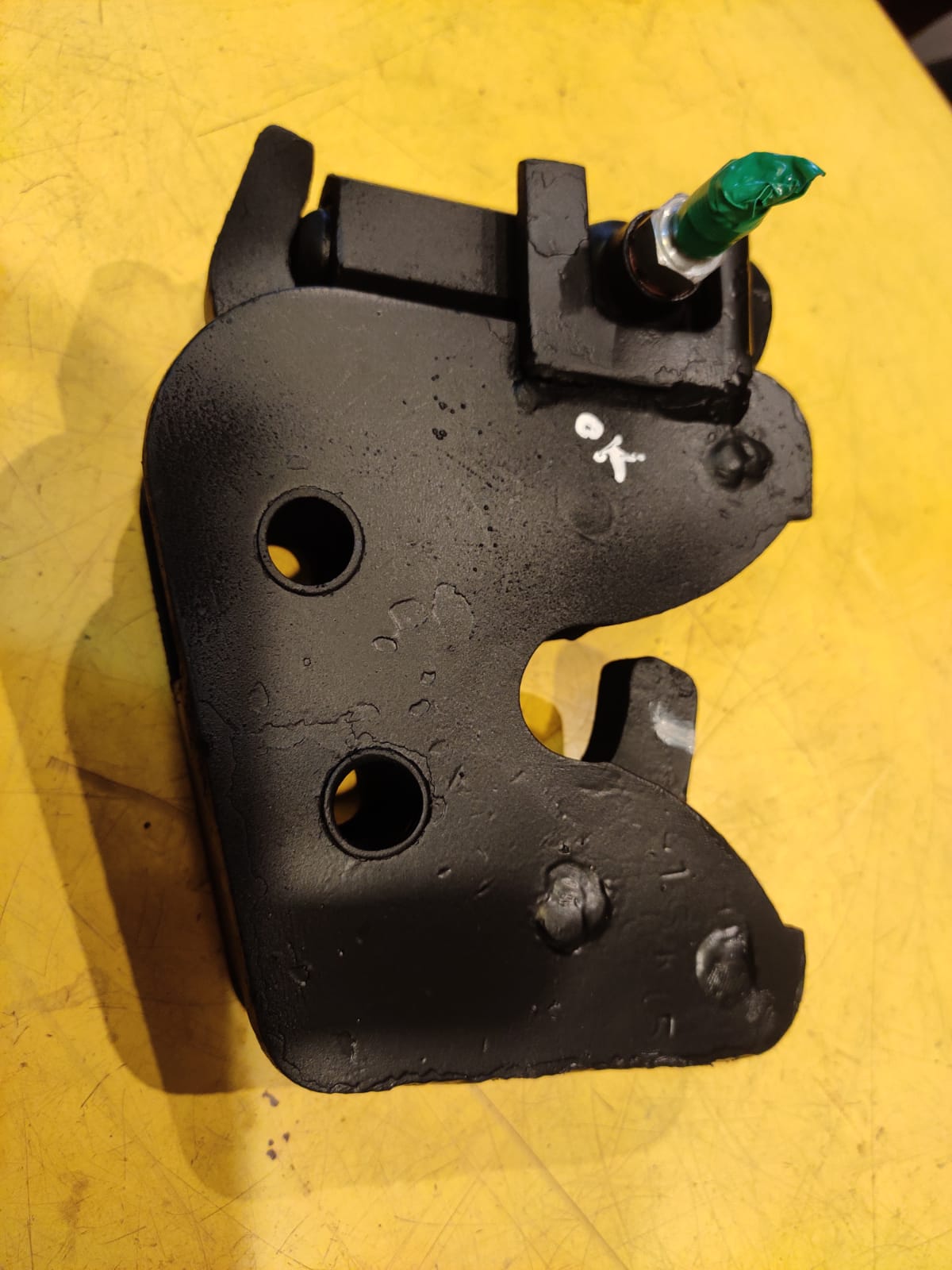Black mechanical component with a green screw on a yellow surface