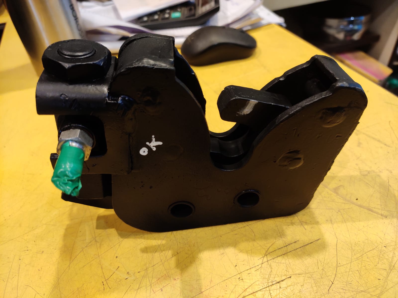 Black mechanical component with a green tag on a yellow surface