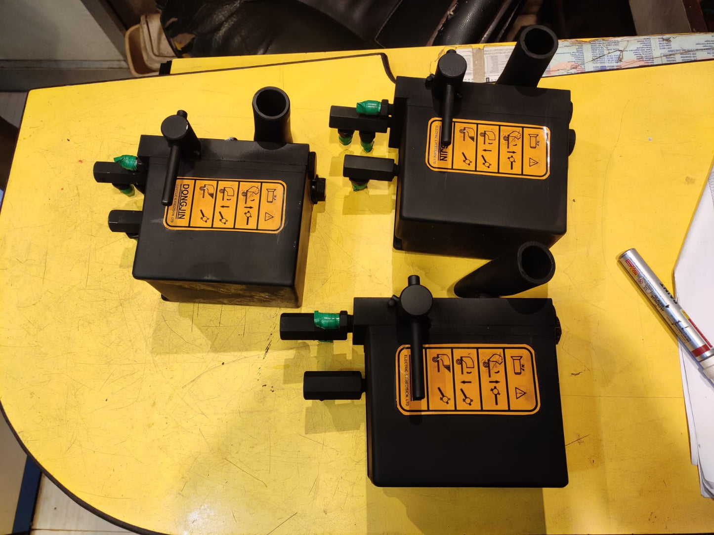 Three black mechanical devices with yellow labels on a yellow surface.