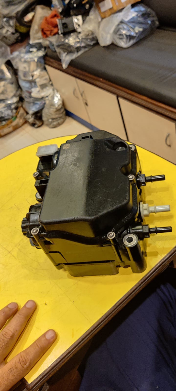 Mechanical component on a yellow surface with a hand for scale
