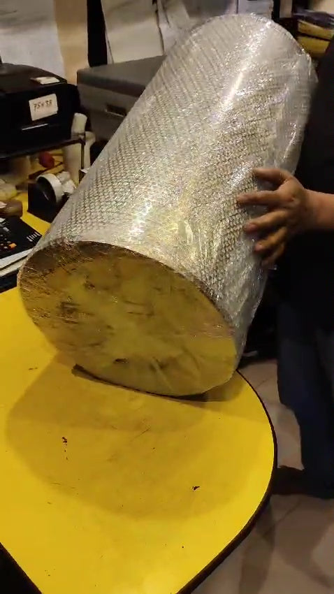 Person holding a large cylindrical object wrapped in bubble wrap on a yellow surface.