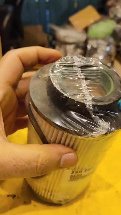 Hand holding a cylindrical oil filter with plastic wrap, blurred background